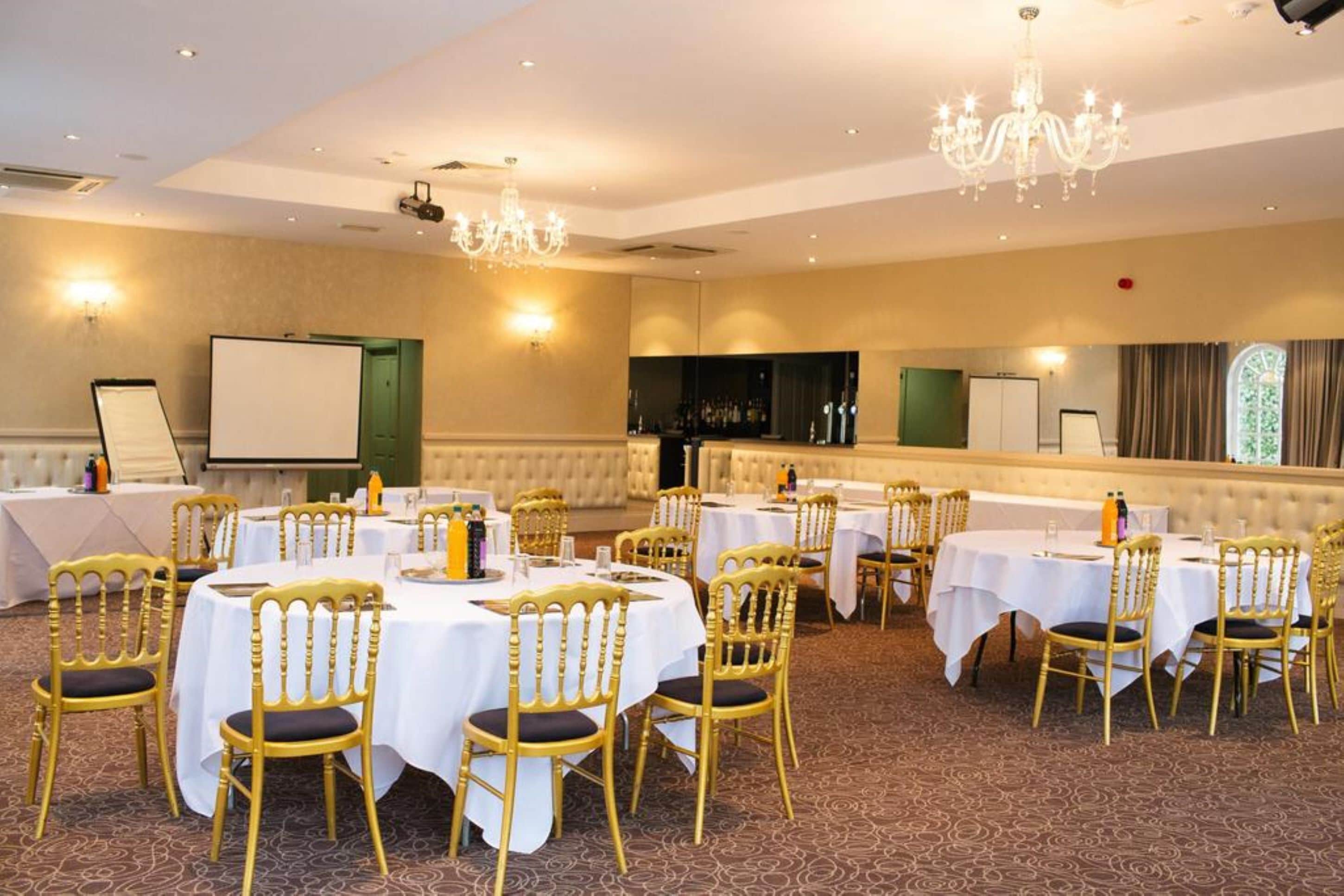 Une salle de banquet avec des tables rondes recouvertes de nappes blanches, des chaises dorées et un lustre.