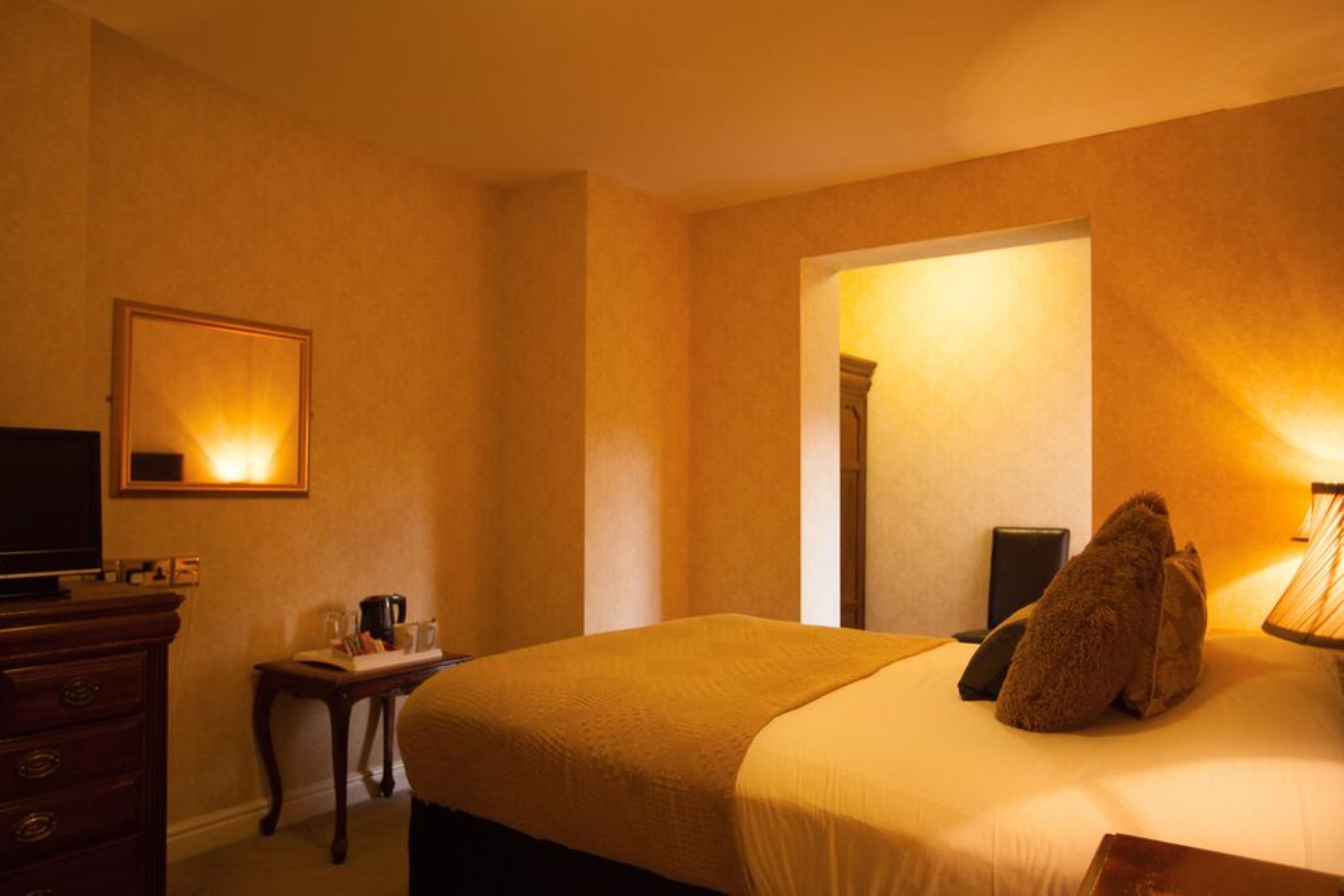 A hotel room with a large bed, a dresser, a television, and a small table with a lamp.