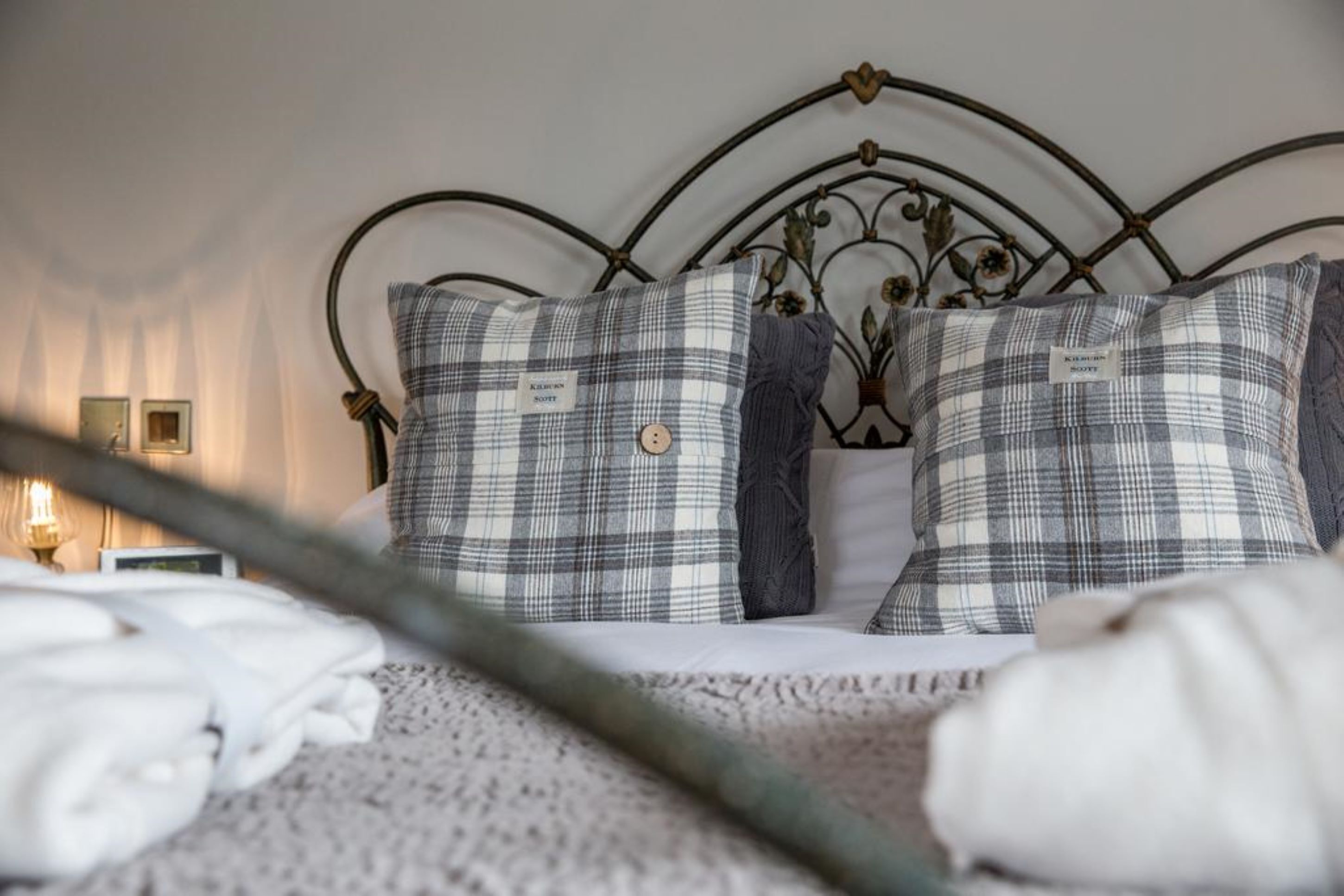 Cama bem arrumada com roupa de cama xadrez e cabeceira de metal.