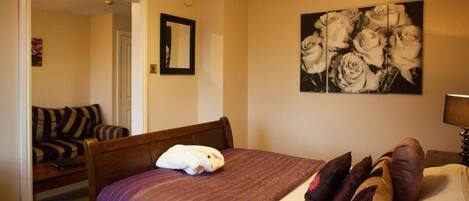 A bedroom with a bed, a chair, a mirror, and a wall-mounted picture of roses.