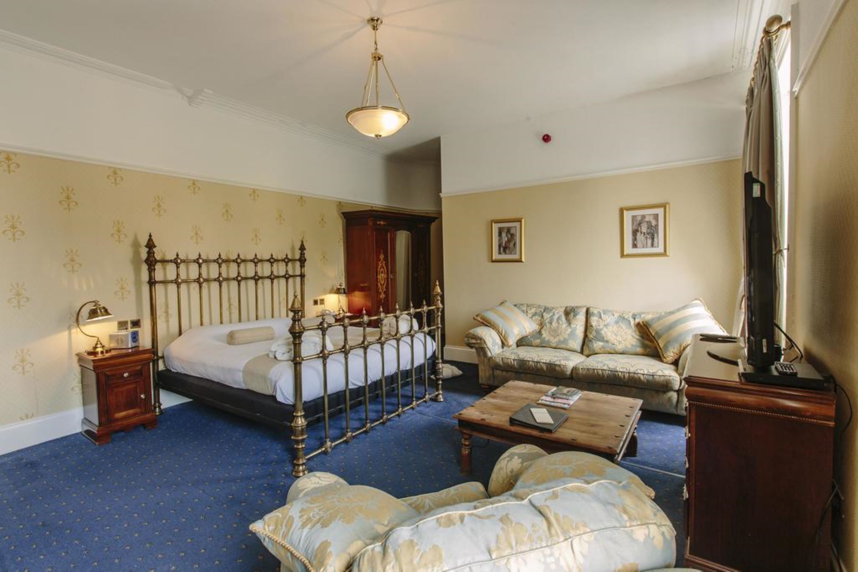 A hotel room with a four-poster bed, a sofa, a coffee table, and a television.