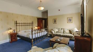 A hotel room with a four-poster bed, a sofa, a coffee table, and a television.