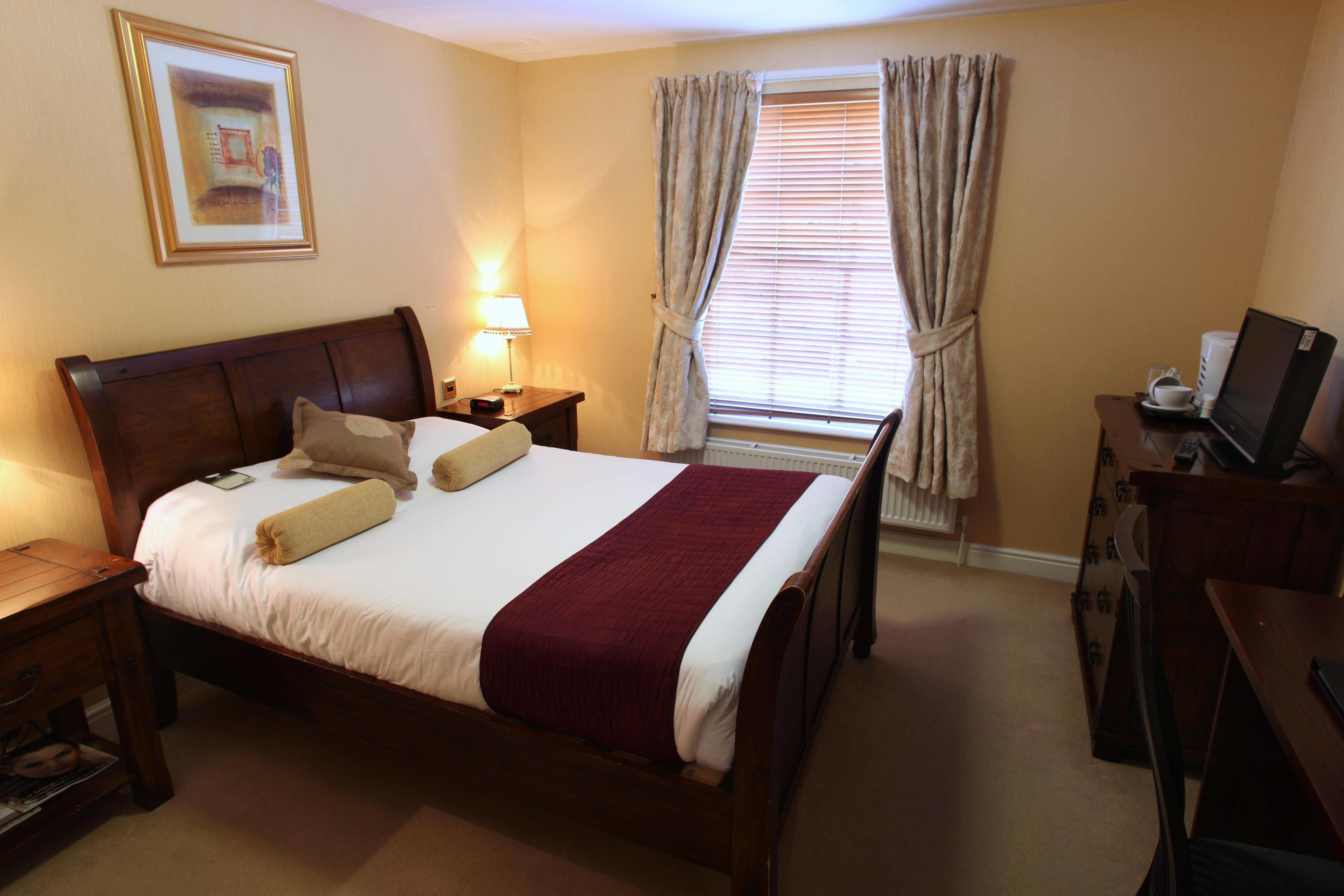 Una habitación de hotel con una cama grande, una mesita de noche con lámpara, un escritorio con ordenador y una ventana con cortinas.