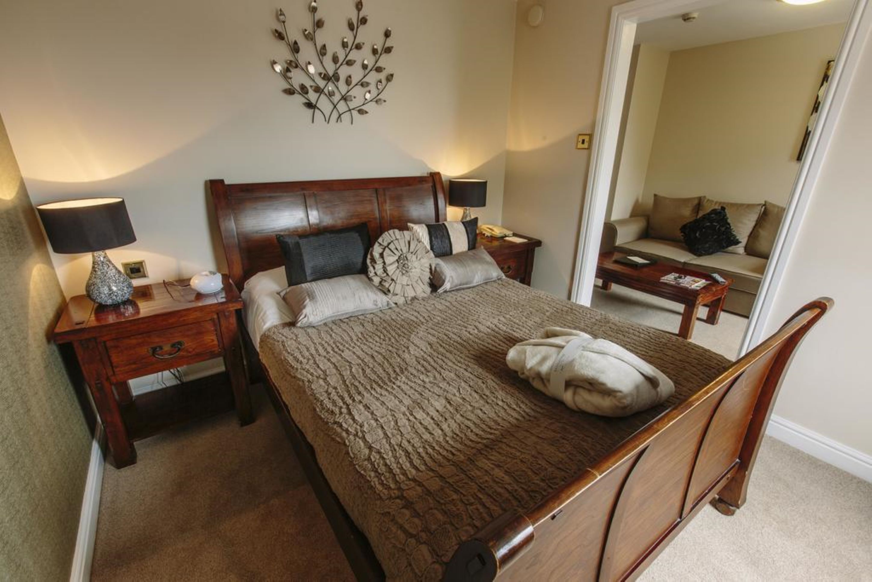 A bedroom with a wooden bed, two bedside tables with lamps, a mirror, and a sofa in the corner.