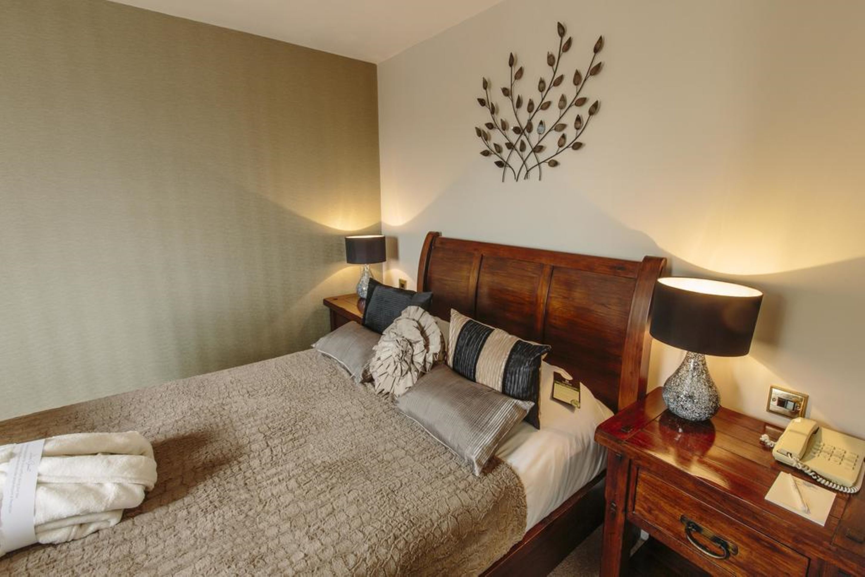 A neatly made bed with a wooden headboard, a bedside lamp, and a wall-mounted decorative piece.