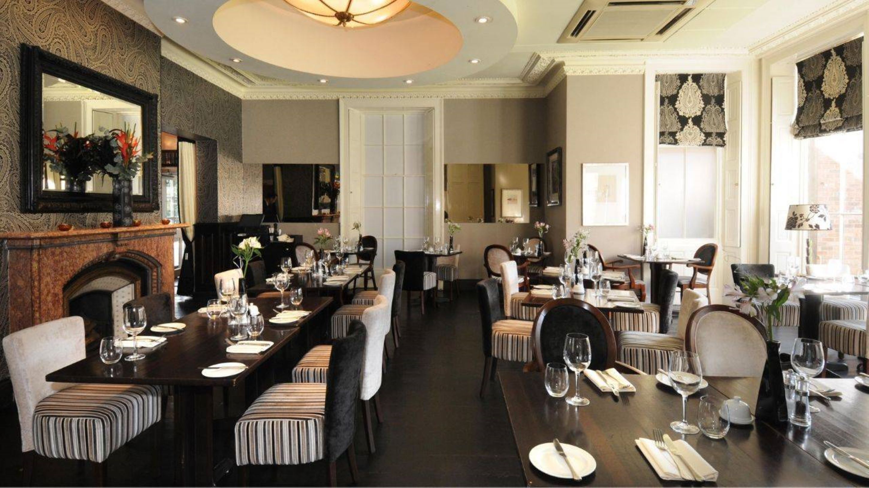 A formal dining room with multiple tables set for service, elegant chairs, and a fireplace.