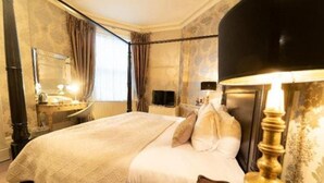 Una habitación de hotel con una cama grande, una mesita de noche, un espejo, una lámpara y una ventana con cortinas.