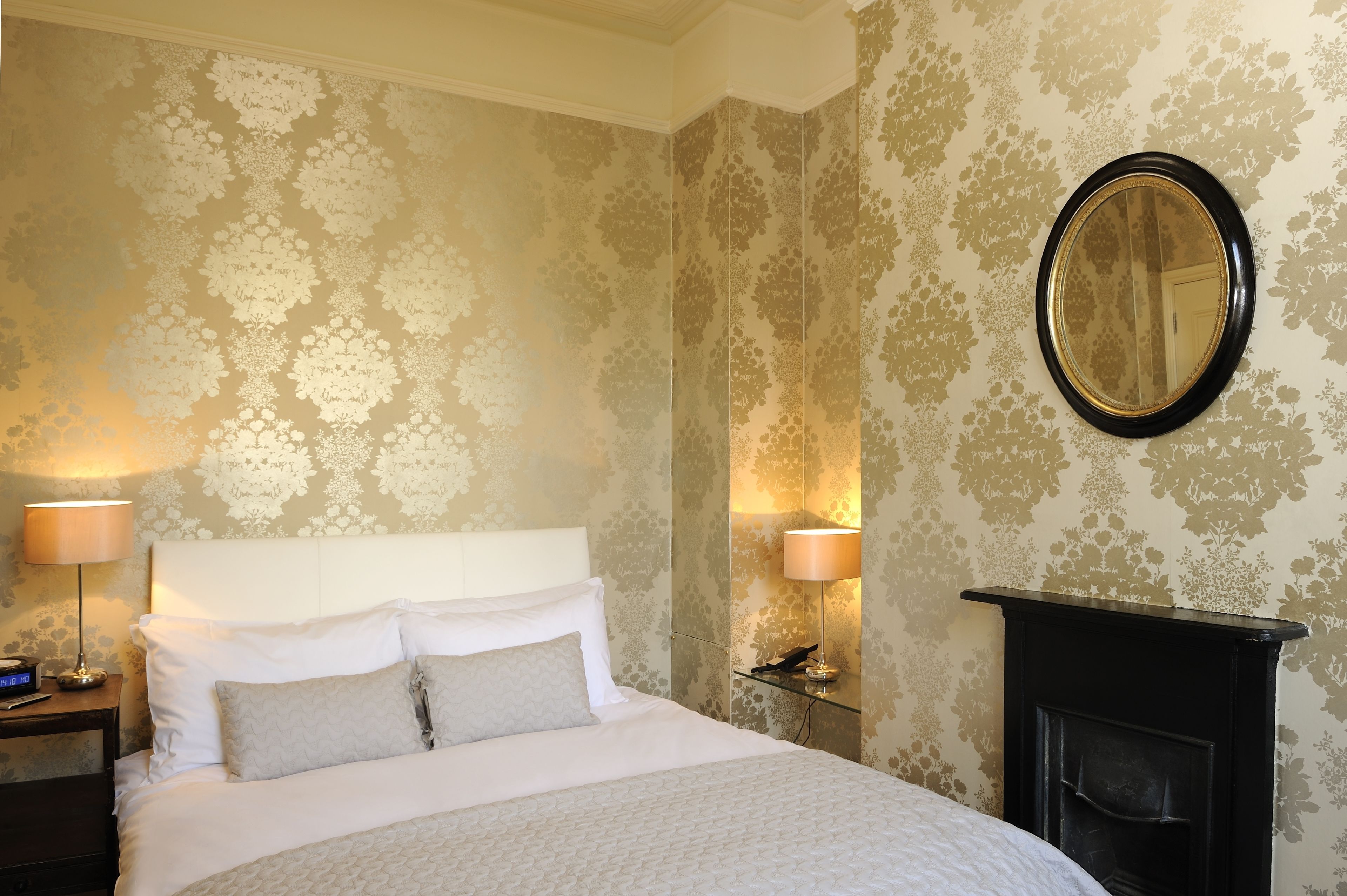A neatly made bed with white linens, a black fireplace, and two wall-mounted lamps.