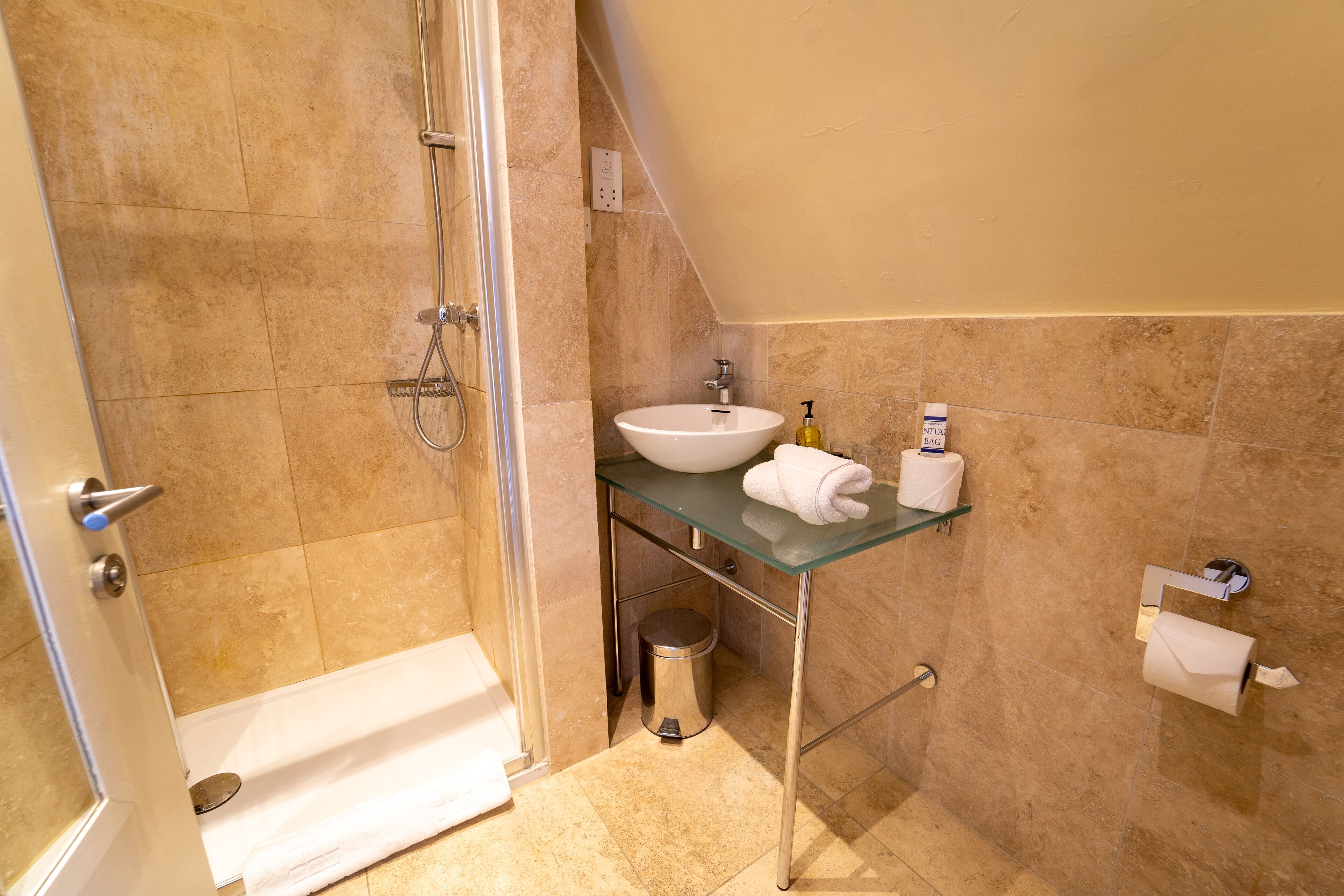 A bathroom with a glass sink, a shower, and a toilet.