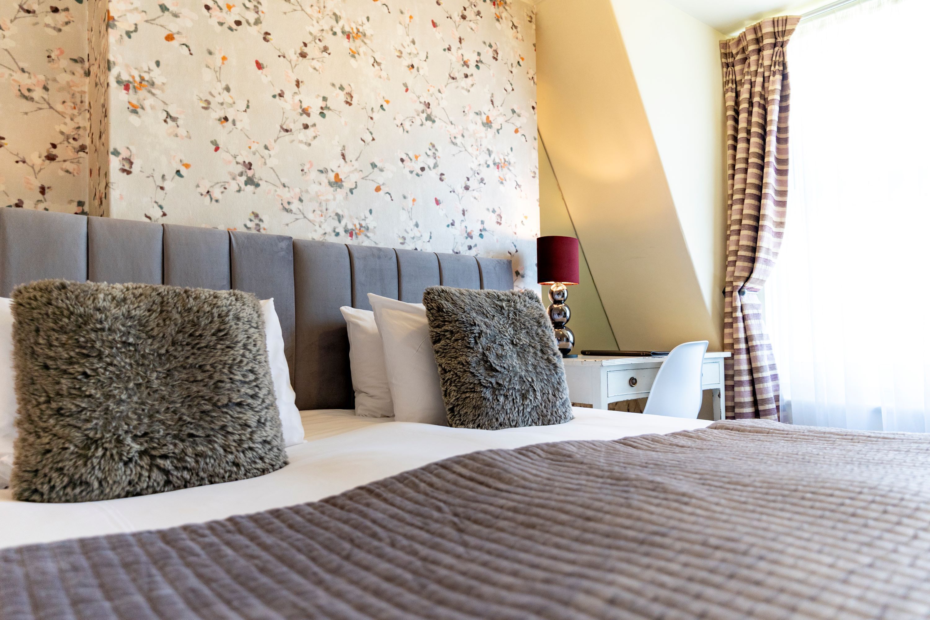 A neatly made bed with a brown quilt, two fluffy pillows, and a grey headboard.