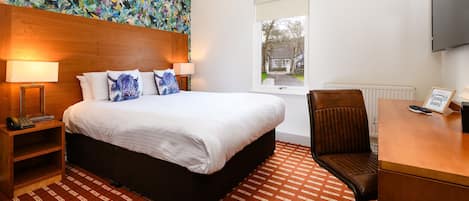 A hotel room with a large bed, two bedside lamps, a desk with a chair, a television, and a window with a view of the outside.