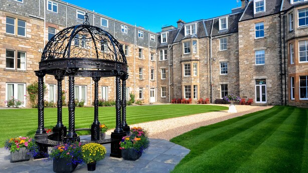 A courtyard with a black gazebo, stone buildings, and well-maintained grass. - Fisher's Hotel (Pitlochry)