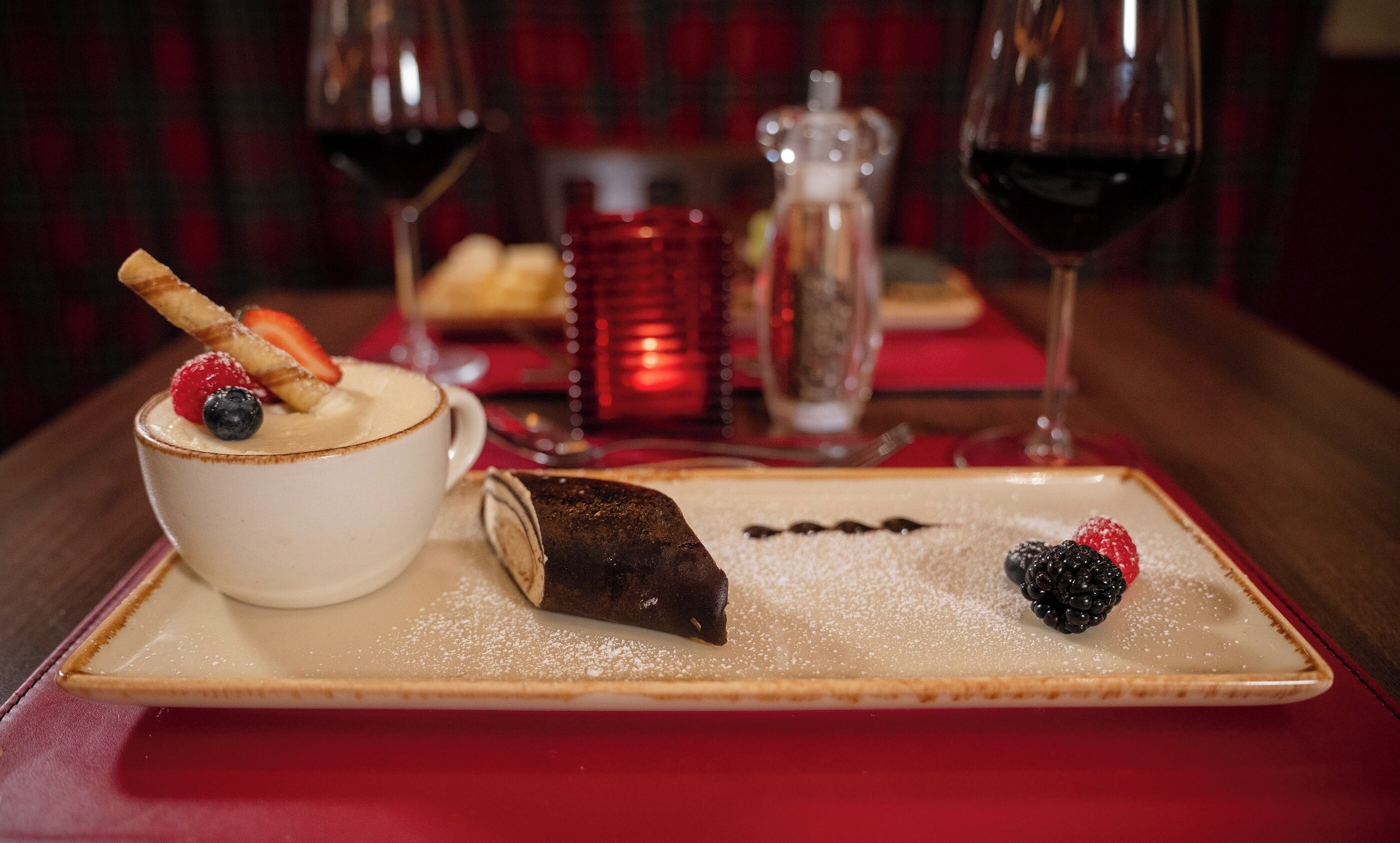A dessert tray with a chocolate roll, berries, and a bowl of dessert with berries and a wafer.