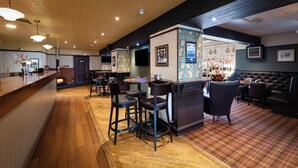 A bar area with wooden flooring, bar stools, a counter with taps, and a fireplace. - Fisher's Hotel (Pitlochry)