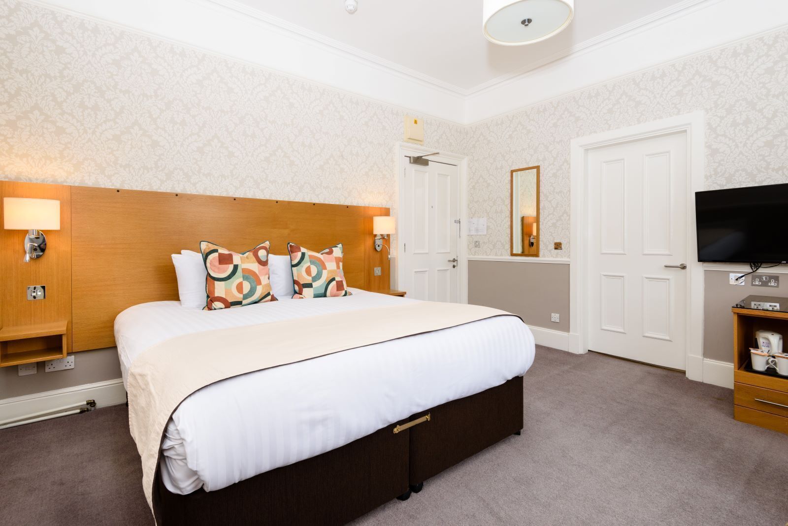 A hotel room with a large bed, two bedside tables with lamps, a television, and a wardrobe.
