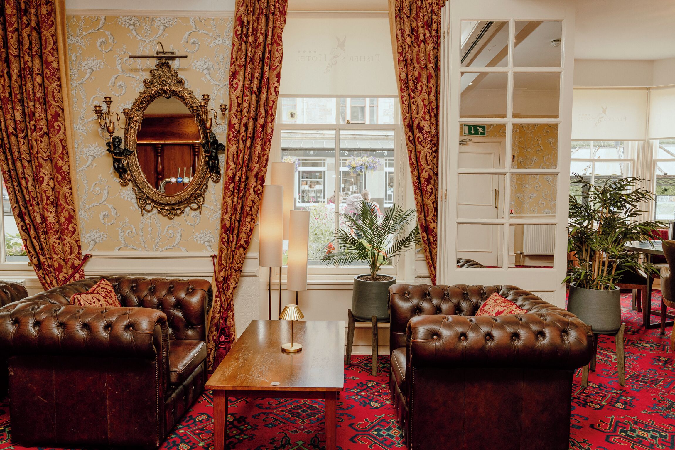 A traditional hotel lobby with leather sofas, a mirror, and potted plants.