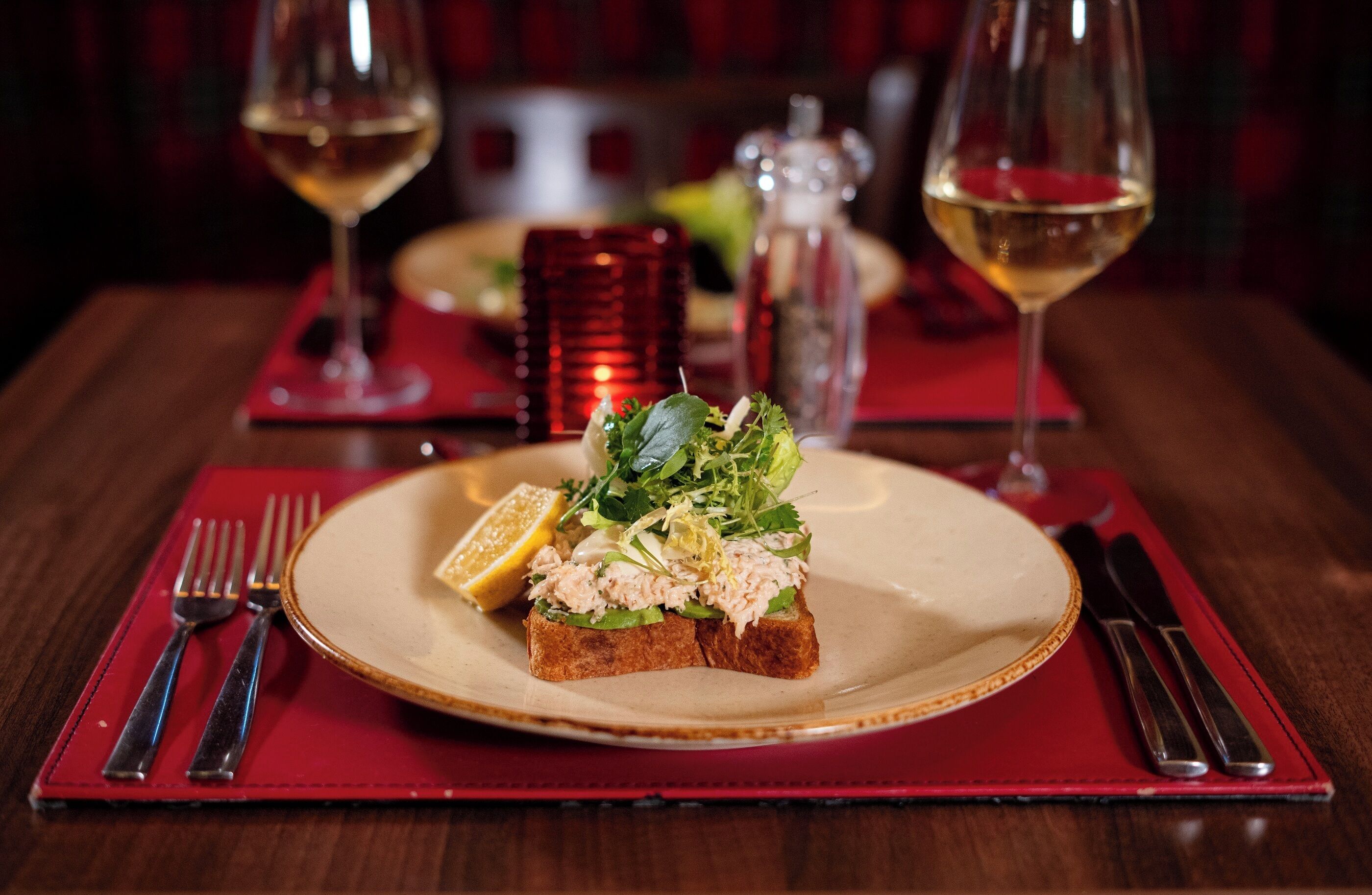 Una mesa de comedor con un plato de comida, una copa de vino y cubiertos.
