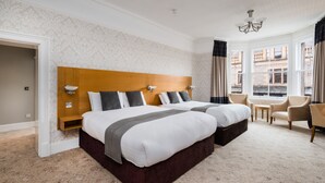 A hotel room with a large bed, a wooden headboard, a small table, and a view of the city through large windows. - Fisher's Hotel (Pitlochry)