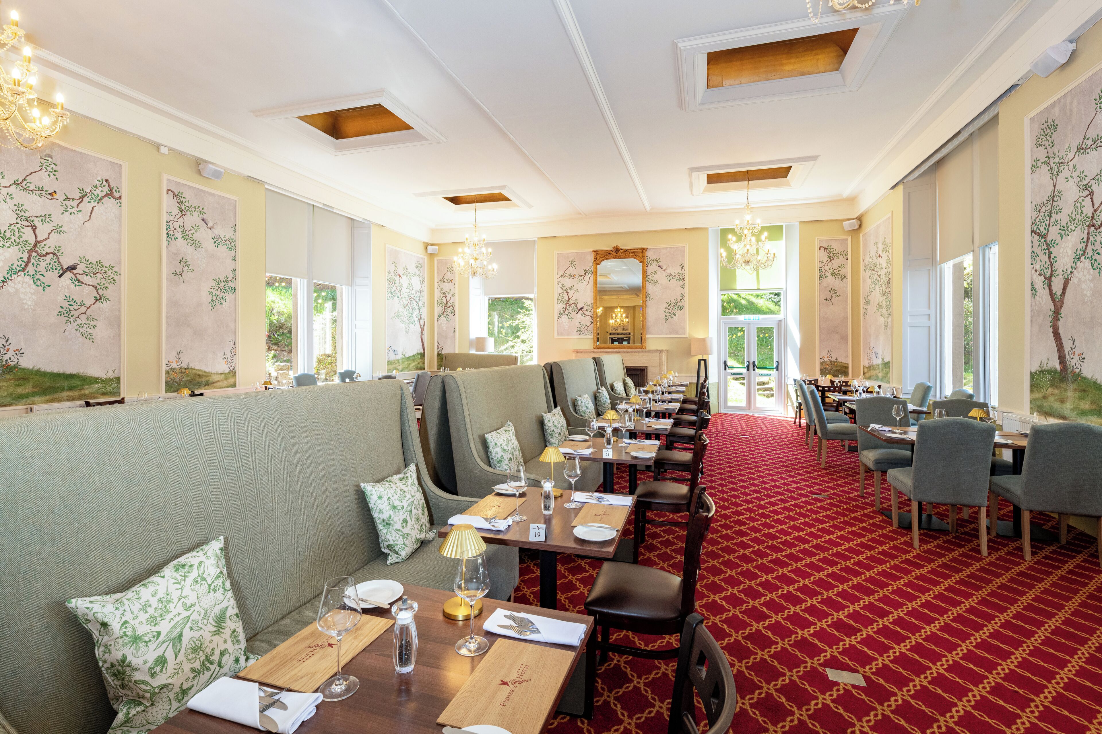Un restaurant avec un tapis rouge, des tables en bois et des banquettes recouvertes d’un tissu vert.