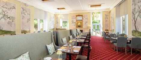 A restaurant with a red carpet, wooden tables, and green upholstered booths.
