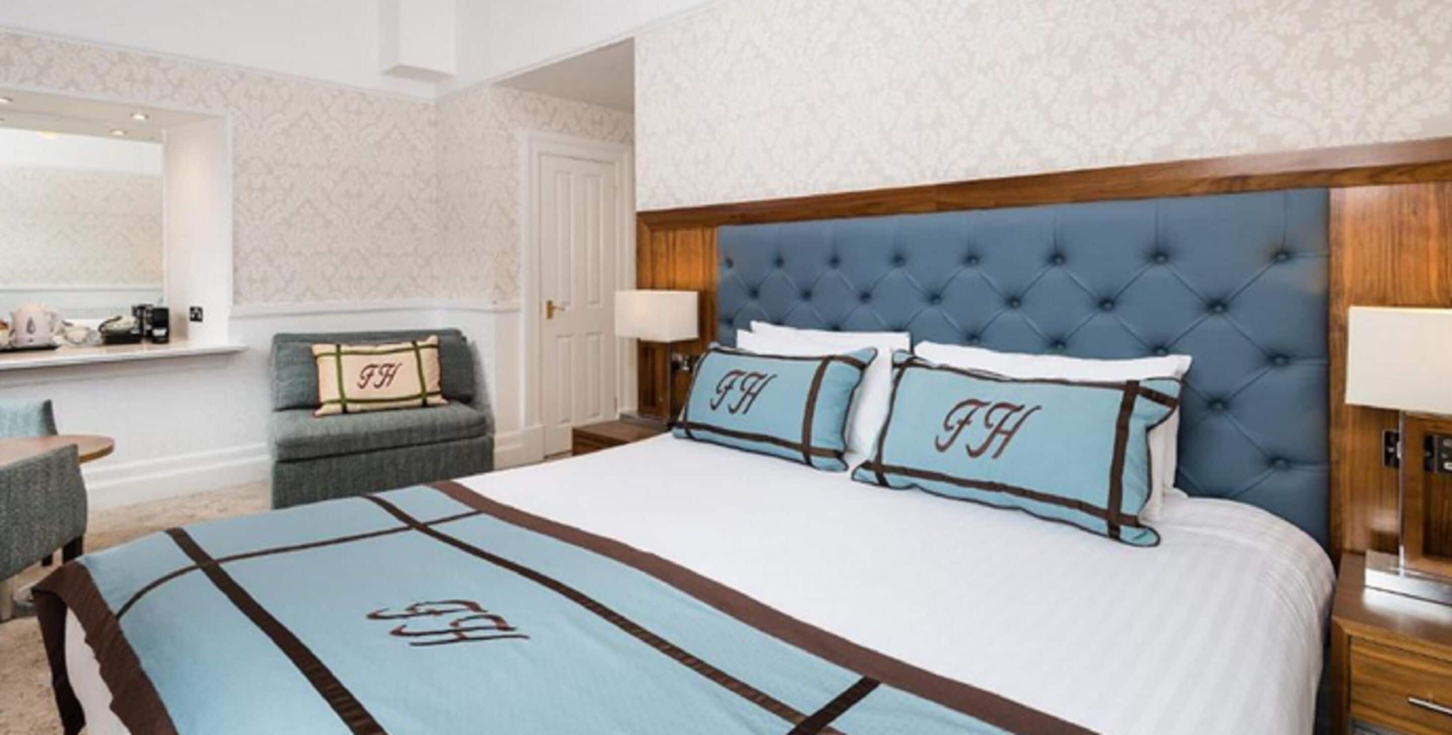 Une chambre d’hôtel avec un grand lit, une tête de lit capitonnée et un canapé agrémenté de coussins assortis.