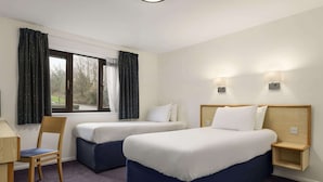 A hotel room with two single beds, a desk, a chair, and a window with curtains.