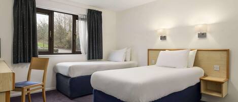 A hotel room with two single beds, a desk, a chair, and a window with curtains.