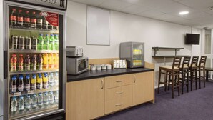 A kitchenette area with a refrigerator stocked with beverages, a microwave, and a small refrigerator. There are wooden cabinets, a countertop, and a dining area with chairs.