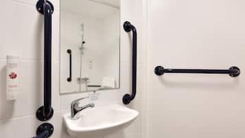 Un baño con un lavamanos blanco, un espejo y barras de apoyo negras.