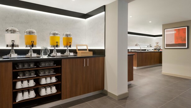 Una cucina moderna con una macchina per caffè integrata, un pensile in legno con tazze e una cornice appesa al muro.