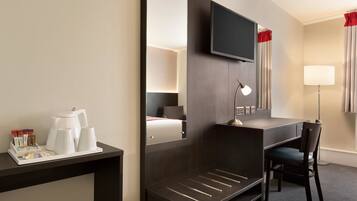 Una habitación de hotel con escritorio, silla, televisor y cama con mesita de noche.