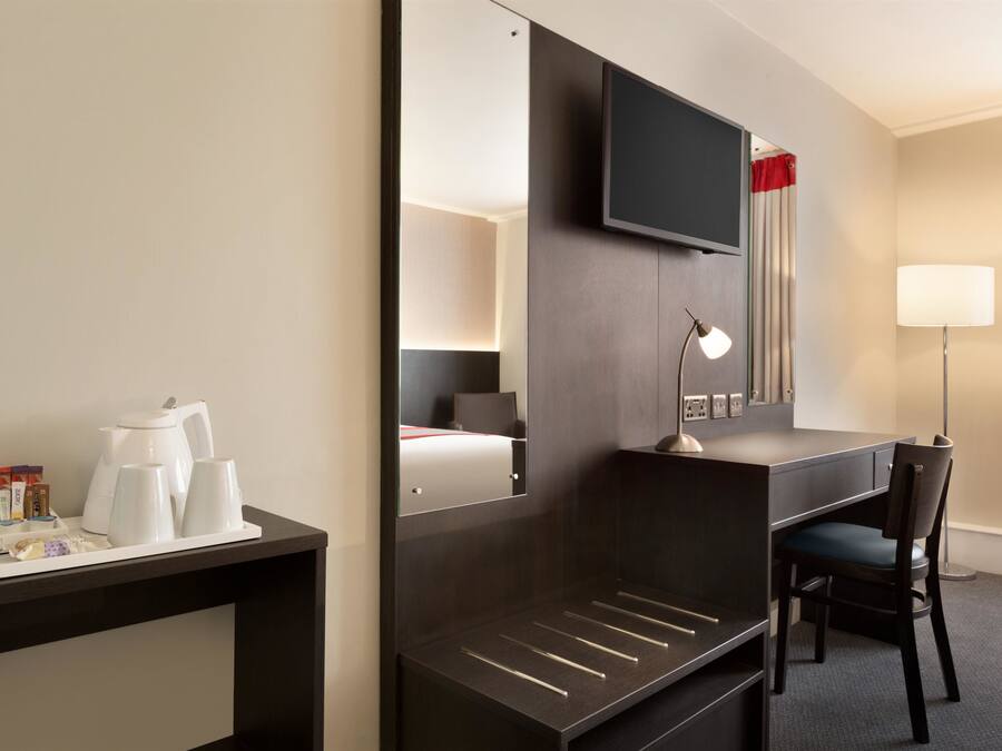 Een hotelkamer met een bureau, stoel, televisie en een bed met nachtkastje.