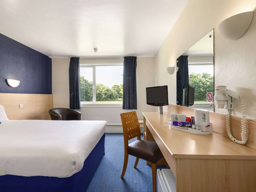 A hotel room with a bed, desk, chair, and a large window with curtains.