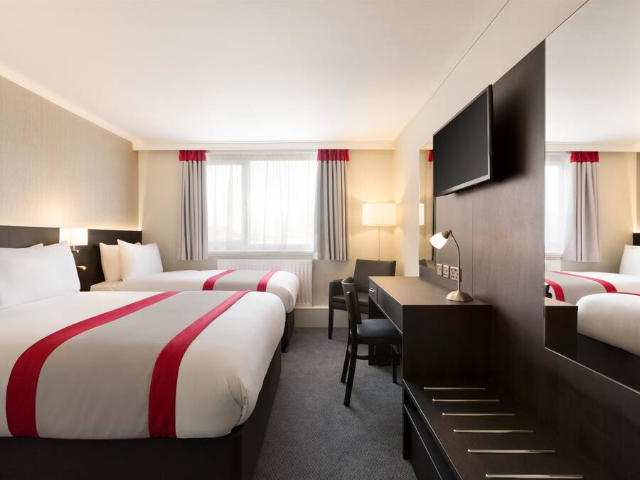 A hotel room with two beds, a desk, a chair, a TV, and a large mirror.