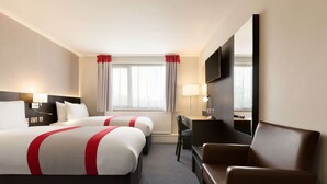 Camera d'albergo con due letti, una scrivania, una sedia, un televisore e una finestra con tende.