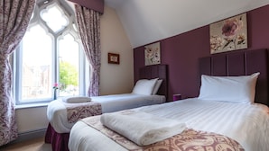 Un dormitorio con dos camas, una ventana con cortinas y una obra de arte floral en la pared.
