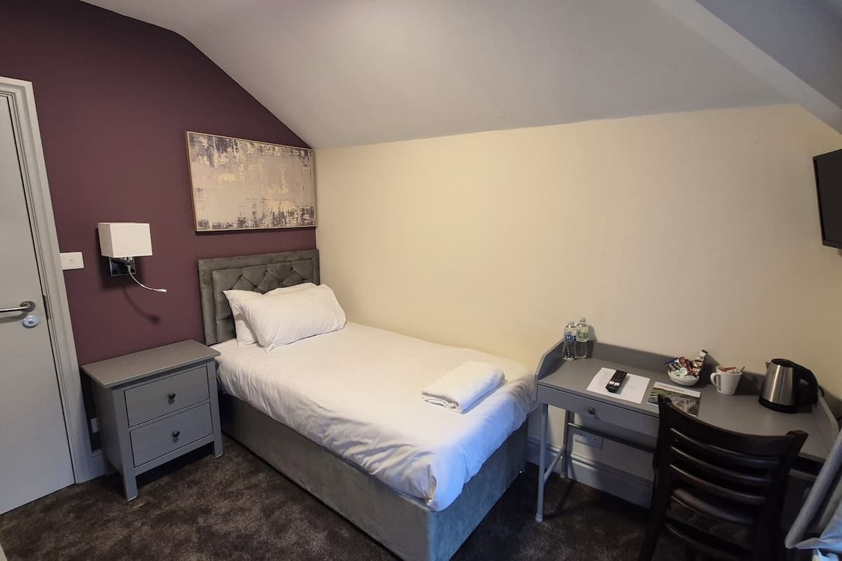 A small, neatly arranged bedroom with a bed, bedside table, desk, and a TV.