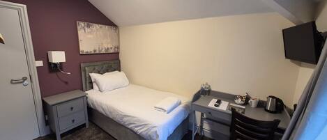 A small, neatly arranged bedroom with a bed, bedside table, desk, and a TV.