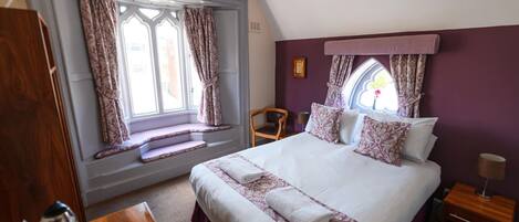 A bedroom with a large bed, a window seat, a chair, and a nightstand.