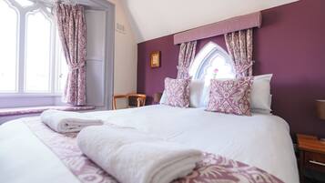 A neatly made bed with patterned bedding, a window with curtains, and a wooden chair.