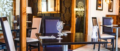 A dining area with tables set for two, featuring modern chairs and a glass wine glass on each table.
