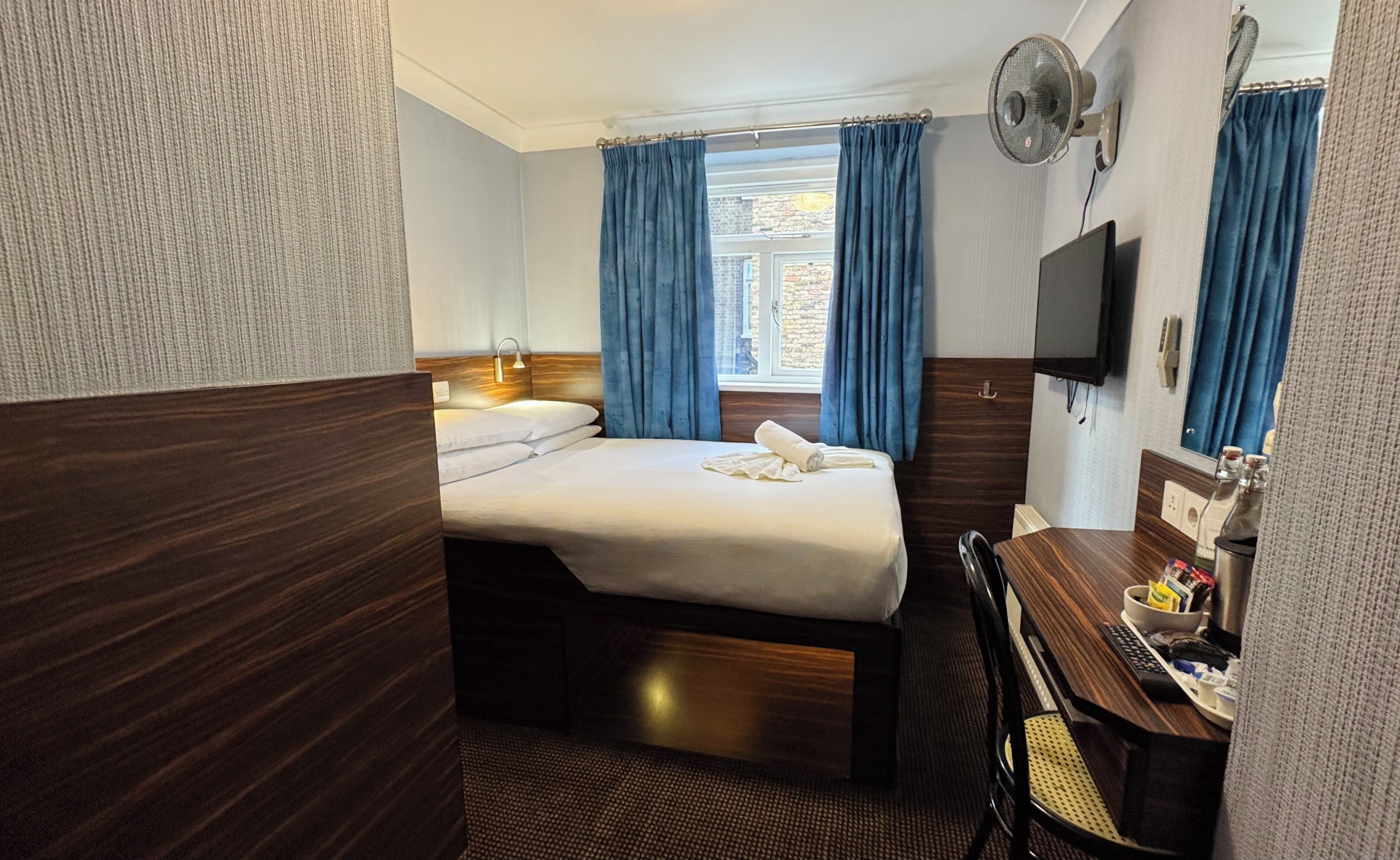 A hotel room with a bed, a desk, a chair, a TV, and a window with curtains.