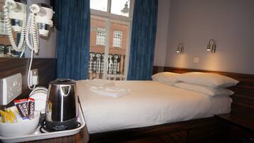 A hotel room with a bed, a coffee maker, a telephone, and a window with blue curtains.