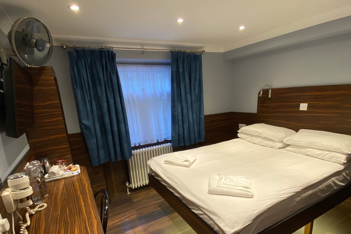 A hotel room with a wooden bed, a desk with a telephone, and a window with blue curtains.