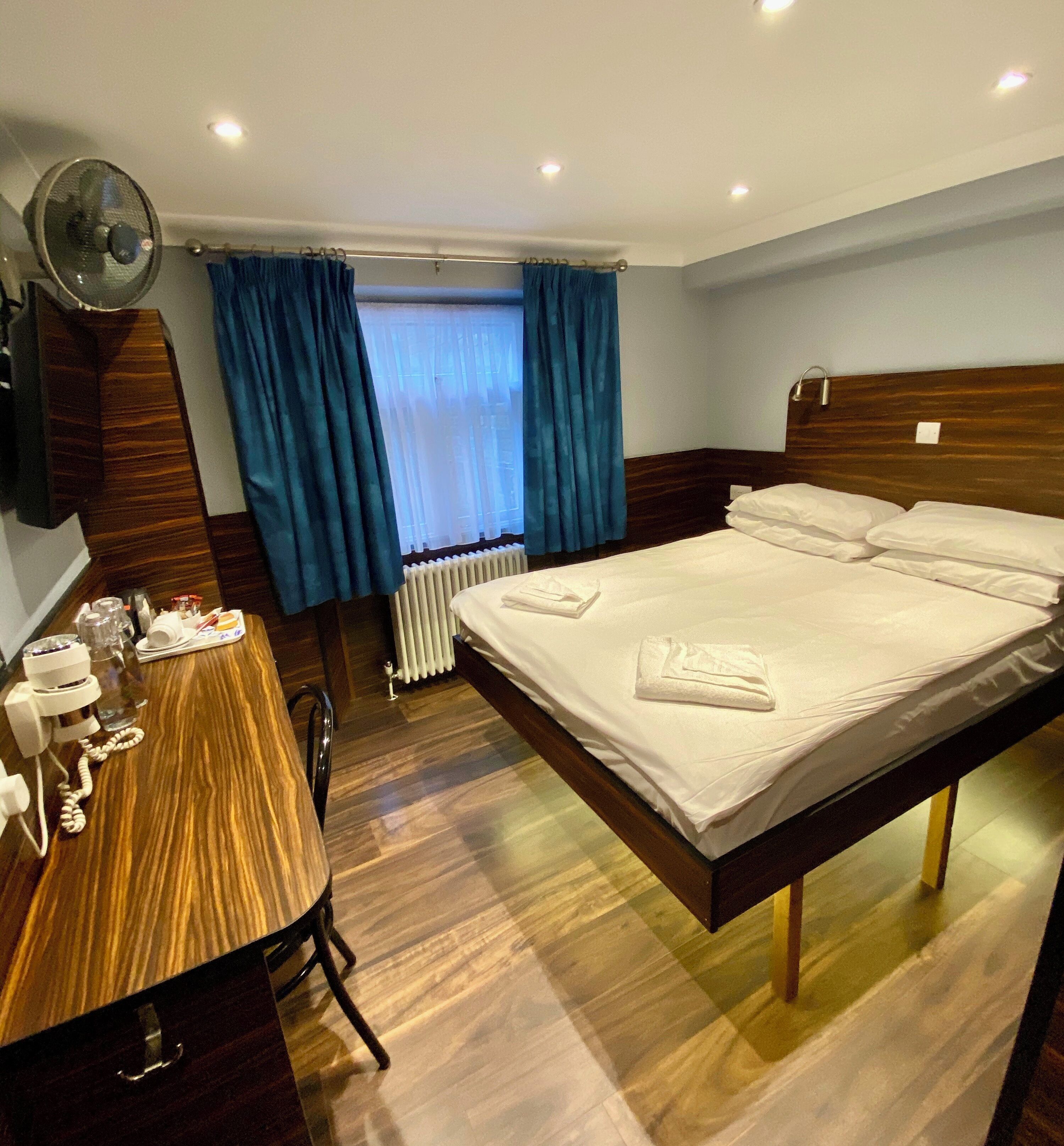 Een hotelkamer met een houten bed, een bureau met telefoon en een raam met blauwe gordijnen.