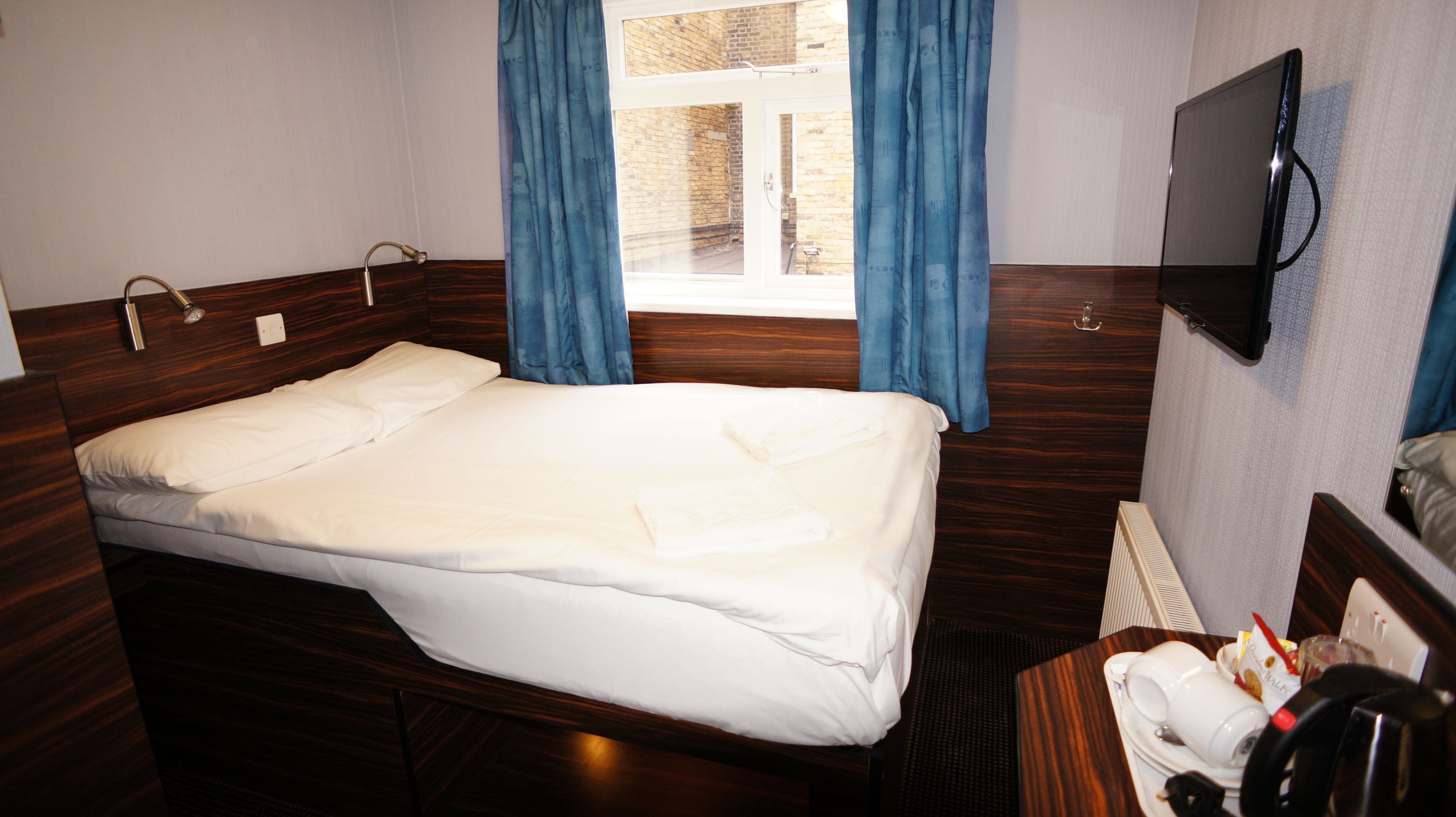 A hotel room with a single bed, a TV mounted on the wall, and a window with curtains.