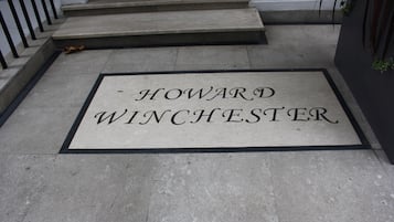 Un felpudo con el nombre "HOWARD WINCHESTER" sobre un suelo de piedra.