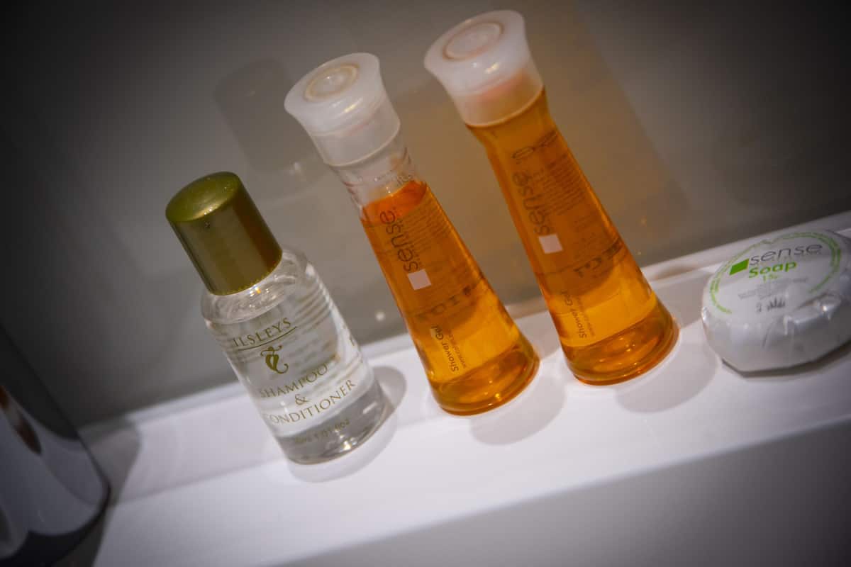 Artigos de higiene em uma prateleira, incluindo uma garrafa de shampoo e condicionador, e duas garrafas de sabonete.