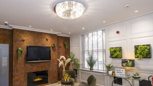 Una sala de estar moderna con chimenea, un televisor grande y una araña. Hay plantas y objetos decorativos en las paredes.
