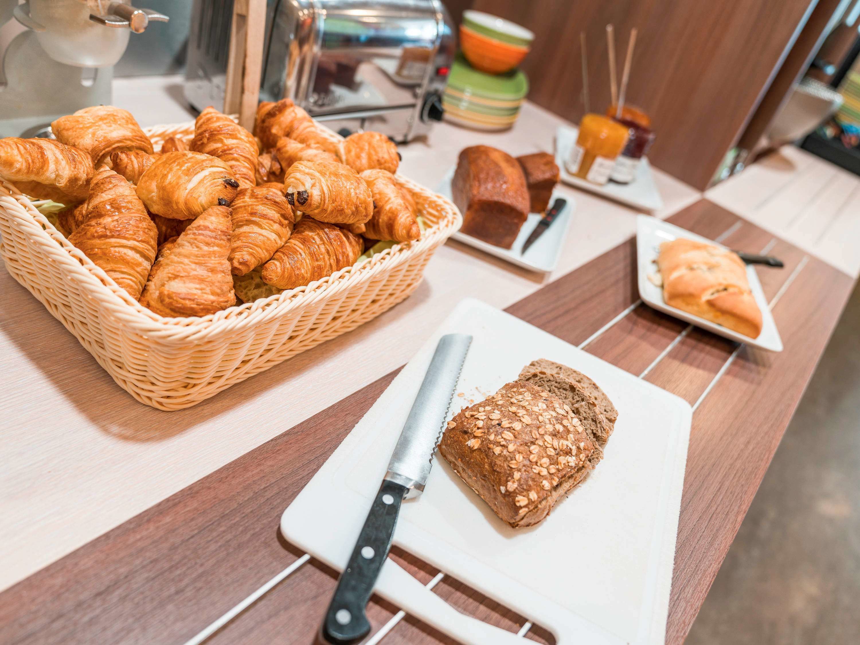 A breakfast buffet with croissants, bread, and a knife on a cutting board.